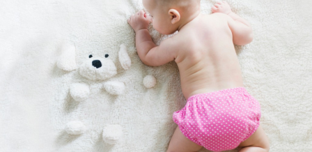 Baby wearing size 1 diapers lying on soft bedding